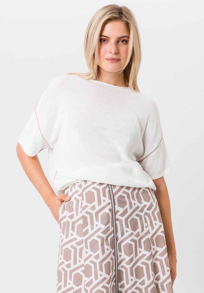 Lichtgewicht witte gebreide top met korte mouwen, gecombineerd met een patroonbeige rok met geometrische ontwerpen en een zichtbare rits.