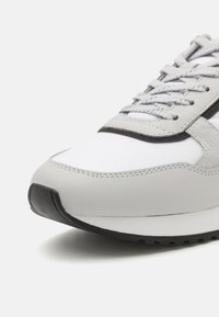 Harmaa lenkkikenkä, jossa on sileä nahkapäällinen ja verkkokangas, teksturoidut harmaat yksityiskohdat, litteät nauhat ja kumipohja, jossa on pito.