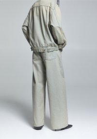 Chaqueta de denim y pantalones de pierna ancha en azul gris claro, con un acabado desgastado, corte relajado y dos bolsillos traseros, combinados con calzado negro.