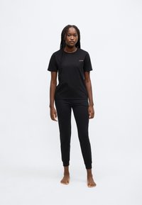 Fekete pamut póló és nadrág szett, rövid ujjú, kerek nyakú, bal mellrészen diszkrét piros logóval. Simább textúrájú, testhezálló kialakítás.