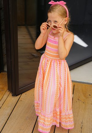 Maxi dress with orange and pink geometric patterns, soft fabric, and ruffled hem. Pair of round sunglasses and pink headband on a child.