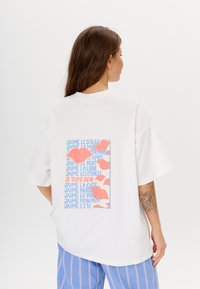 Witte oversized t-shirt met korte mouwen, voorzien van een kleurrijke grafische print in roze en blauw op de achterkant, met verschillende zinnen.