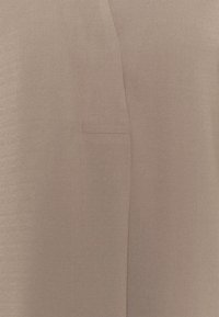 Tissu beige avec une couture subtile et une couture verticale, montrant un petit détail rectangulaire cousu près du centre.