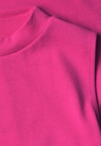 Gros plan d'un haut sans manches rose vif montrant le col et la couture d'épaule avec une texture de tissu lisse.