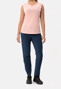 Light pink sleeveless top with a small keyhole detail; paired with dark blue, lightweight, water-resistant pants and black hiking shoes.