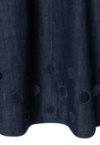 Dark blue denim fabric with embroidered and cut-out circular patterns near the hem, draped with soft folds.