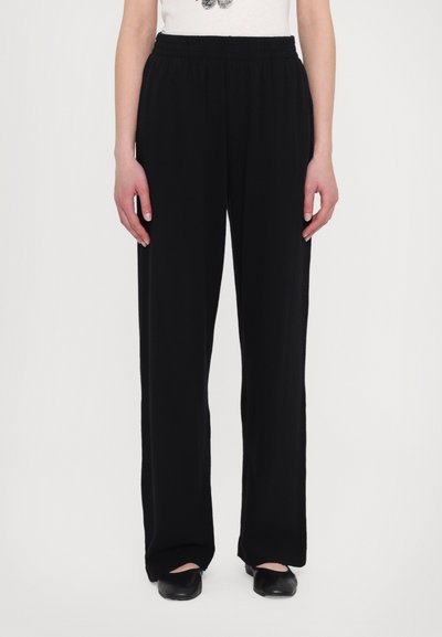 Black wide-leg trousers with an elastic waist, made from soft fabric, featuring a smooth texture and a relaxed fit. Accompanied by black flats.