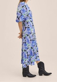 Květinové midi šaty s krátkými nabíranými rukávy, s velkými modrými a zelenými květinami na černém pozadí. V kombinaci s černými kovbojskými botami.
