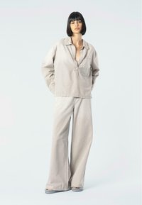 Camicia oversized grigio chiaro con colletto a scollo a V e taschino frontale, abbinata a pantaloni grigi a gamba larga, entrambi realizzati in un morbido tessuto testurizzato.