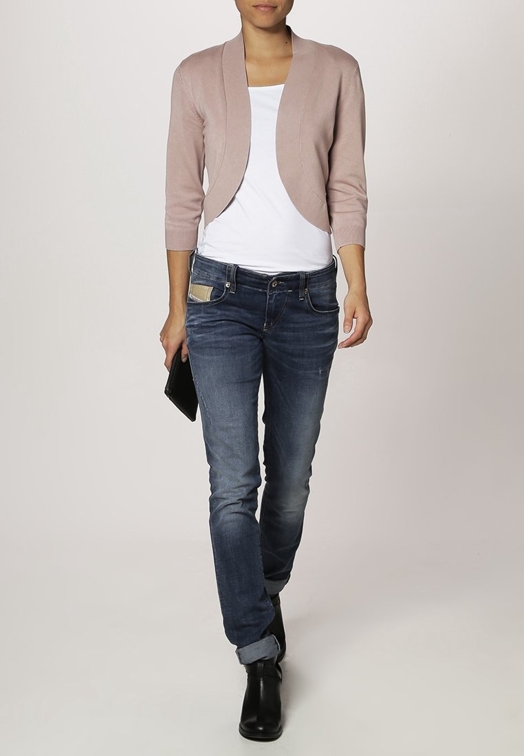 Ljusrosa kort kofta med trekvartsärmar över en vit topp, kombinerad med mörkblå jeans och svarta ankelboots.