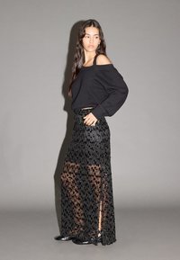 Maglione nero a costine con design scivolato sulle spalle abbinato a una gonna lunga nera trasparente con motivi intricati simili a perline e spacchi.