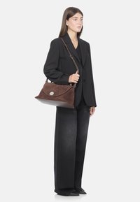 Borsa a tracolla in suede marrone con pattina curvata, accento in metallo del logo e base in pelle marrone; presenta una tracolla regolabile.