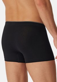 Schwarze Boxershorts mit tailliertem Design, weichem Griff und kontrastierendem Bündchen. Der Stoff wirkt glatt und dehnbar.