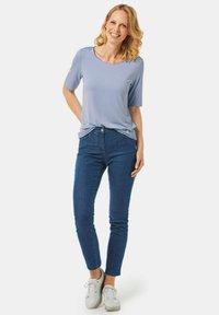 Helles blaues kurzärmeliges Oberteil mit rundem Ausschnitt, kombiniert mit dunkelblauen Skinny-Jeans und weißen Sneakers. Glatte Stoffqualität und lässige Passform.