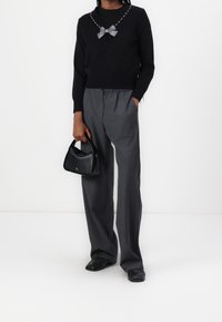Czarny sweter z detalem z kokardą z kryształków, szare spodnie o szerokich nogawkach oraz mała czarna torebka. Modelka ma na sobie czarne buty.