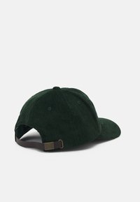 Grønn corduroy caps med buet skjerm, teksturert overflate, justerbar brun stropp bak og små ventilasjonshull på sidene.