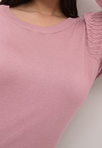 Pink knit top featuring a ribbed neckline and textured puff sleeves with a wavy pattern. Soft, lightweight fabric with a smooth finish.