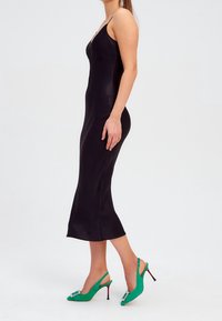Schwarzes Satin-Überkleid mit Spaghetti-Trägern, figurbetonter Passform und ausgestellt geschnittenem Saum. Kombiniert mit grünen Wildleder-Slingback-Absätzen mit dekorativen Akzenten.