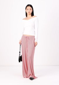 White long-sleeve off-shoulder top paired with red and white striped wide-leg pants, featuring a drawstring and black handbag. Black slip-on shoes.