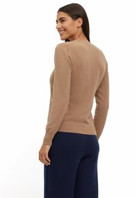 Beige gebreide trui met een ronde halslijn, geribbelde manchetten en zoom, gladde textuur, gecombineerd met marineblauwe wijde broek. Achteraanzicht weergegeven.