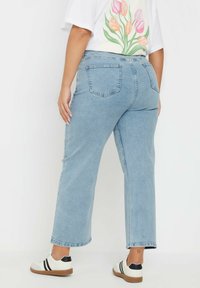 Jeans de denim azul claro con corte recto, cinco bolsillos y cintura de altura media. Llevados con una camiseta blanca y zapatillas casuales.