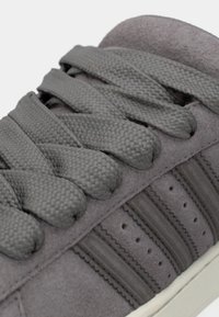 Γκρι σουέντ αθλητικό παπούτσι με υφασμένους γκρι κορδόνια, διαθέτει τρεις οριζόντιες ρίγες, οπές στο πλάι και λευκή λαστιχένια σόλα.