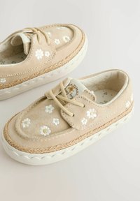 Chaussures en daim beige avec broderie florale blanche, semelle intermédiaire en jute tressé et semelle extérieure en caoutchouc blanc. Design à lacets avec doublure en tissu.
