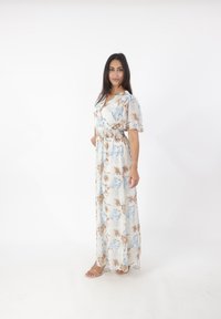 Floral Maxi-Kleid aus leichtem Stoff, mit V-Ausschnitt, kurzen Puffärmeln und elastischem Taillenbund. Die Farben umfassen Blau, Braun und Creme.