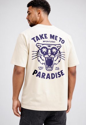 Mann trägt ein cremefarbenes T-Shirt mit einer Grafik eines Tigers mit offenem Maul und Sonnenbrille, in der Palmen und der Text "Take me to paradise, chill out all day." zu sehen sind.