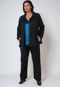 Black jacket with large buttons, paired with a teal top and black pants. The fabric appears smooth, with a tailored fit and structured collar.