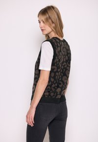 Schwarzer Strickwesten mit braunem Leopardenmuster, gestrickte Textur, gerippter Halsausschnitt und Saum, getragen über einem weißen T-Shirt, kombiniert mit dunklen Jeans.