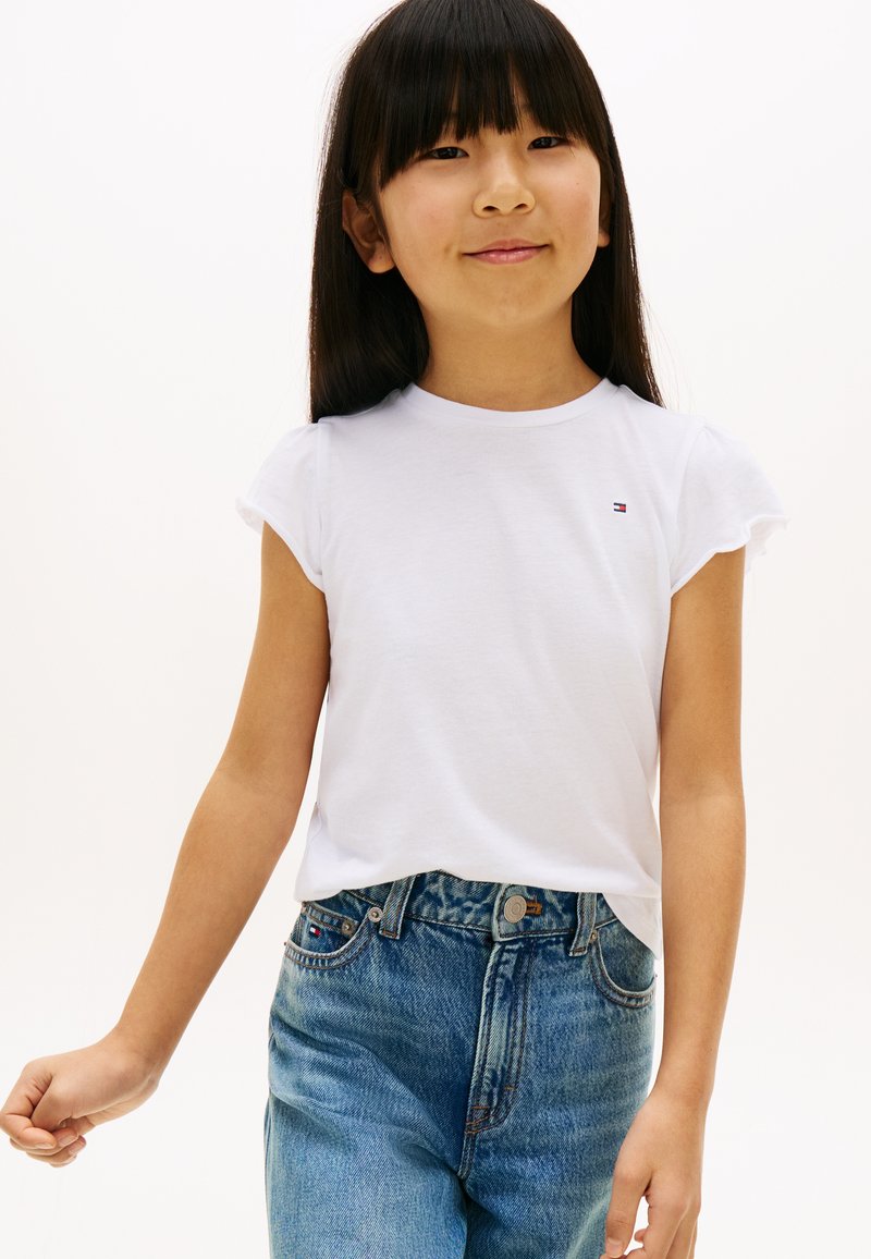 Weißes Baumwoll-T-Shirt mit kurzen Ärmeln, Logodetail auf der Brust, kombiniert mit hoch taillierten, stark verwaschenen blauen Denim-Jeans.