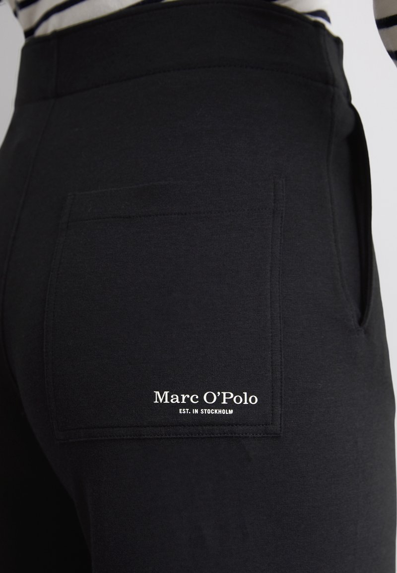 Czarne dresy z tylną kieszenią. Wyposażone w białe logo "Marc O'Polo EST. W Sztokholmie." Miękka tkanina o gładkiej fakturze.