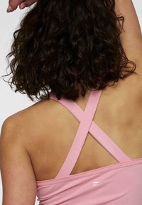 Top deportivo rosa con tirantes cruzados, confeccionado en un material suave. Presenta un logotipo sutil en la parte posterior y una textura lisa.