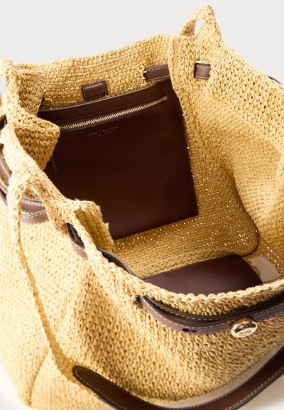 Ανοιχτή υφασμένη τσάντα από άχυρο με καφέ δερμάτινη εσωτερική θήκη με χρυσό φερμουάρ και λογότυπο Tory Burch, καθώς και δερμάτινη επένδυση με χρυσό κουμπί.