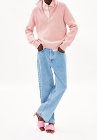 Pull côtelé rose clair avec fermeture à moitié zip, jean large en denim bleu clair, et sandales à talons roses complètent la tenue.