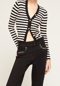 Randig svart och vit cardigan med långa ärmar, med v-ringning och synliga knappar. Kombinerad med svarta byxor prydda med dekorativa nitar vid fickorna.