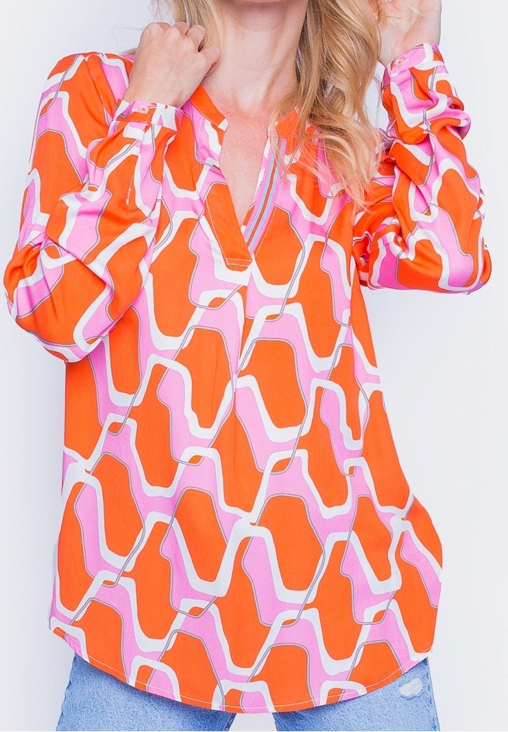 Femme portant un chemisier ample à manches longues avec un motif géométrique audacieux orange, rose et blanc, associé à un jean bleu clair.