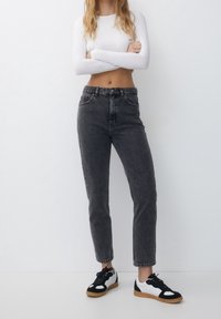 Jeans negros de cintura alta con un ligero ajuste, hechos de denim. Combinados con zapatillas negras y blancas con suela de goma.