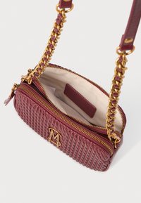 Liten vinröd crossbody-väska med flätad textur, guldfärgad hårdvara, dragkedjestängning och en enda kedjestropp. Neutral tyginteriör med en etikett.