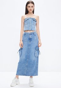 Denim crop top with button closure, paired with a long denim skirt featuring cargo pockets. Worn with white sneakers. Light blue color.