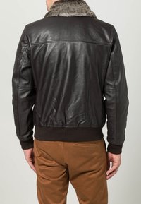 Musta nahkainen pommittaj jacket, jossa on tekoturkista tehty kaulus, ribbitoitu vyötärö ja pitkät hihat. Takana on sileä pinta ja hienovaraiset ompelu yksityiskohdat.
