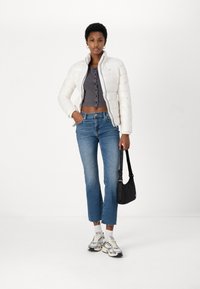 Hvit pufferjakke, grå cropped topp med knapper, blå straight-leg jeans, svart skulderveske og sølvfargede joggesko med hvite sokker.