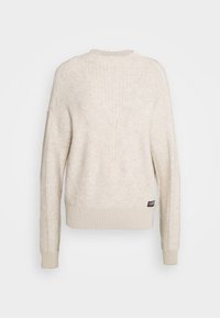 Pull tricoté couleur crème avec un ourlet et des poignets côtelés, présentant un motif texturé en forme de V au dos et une petite étiquette de marque.