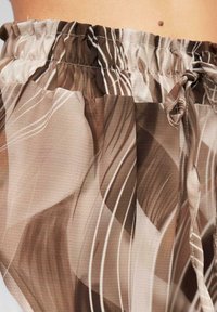 Brown and beige patterned fabric with a gathered waistband and drawstring. Smooth texture with flowing, wavy lines and layered design.