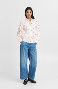Cămașă albă cu imprimeu floral roșu, mâneci lungi și manșete, combinată cu blugi largi de culoare albastră deschisă și mocasini negri.
