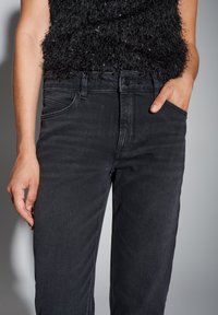 Jean en denim noir à coupe slim, doté d'un design classique à cinq poches et d'un léger effet délavé. Texture lisse ; quincaillerie noire assortie.