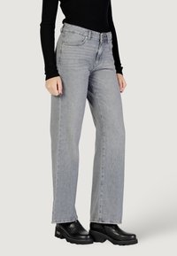 Jeans grigi alti in vita con un design a gamba dritta, caratterizzati da un leggero lavaggio e cinque tasche, abbinati a stivaletti neri con suola piatta e spessa.