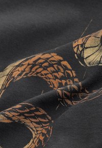 Tissu noir avec des écailles de serpent détaillées de couleur cuivre et des segments imprimés sur sa surface.