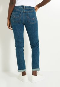 Jeans de mezclilla azul oscuro con un diseño ajustado, puños doblados y dos bolsillos traseros con detalles de costura curvada.